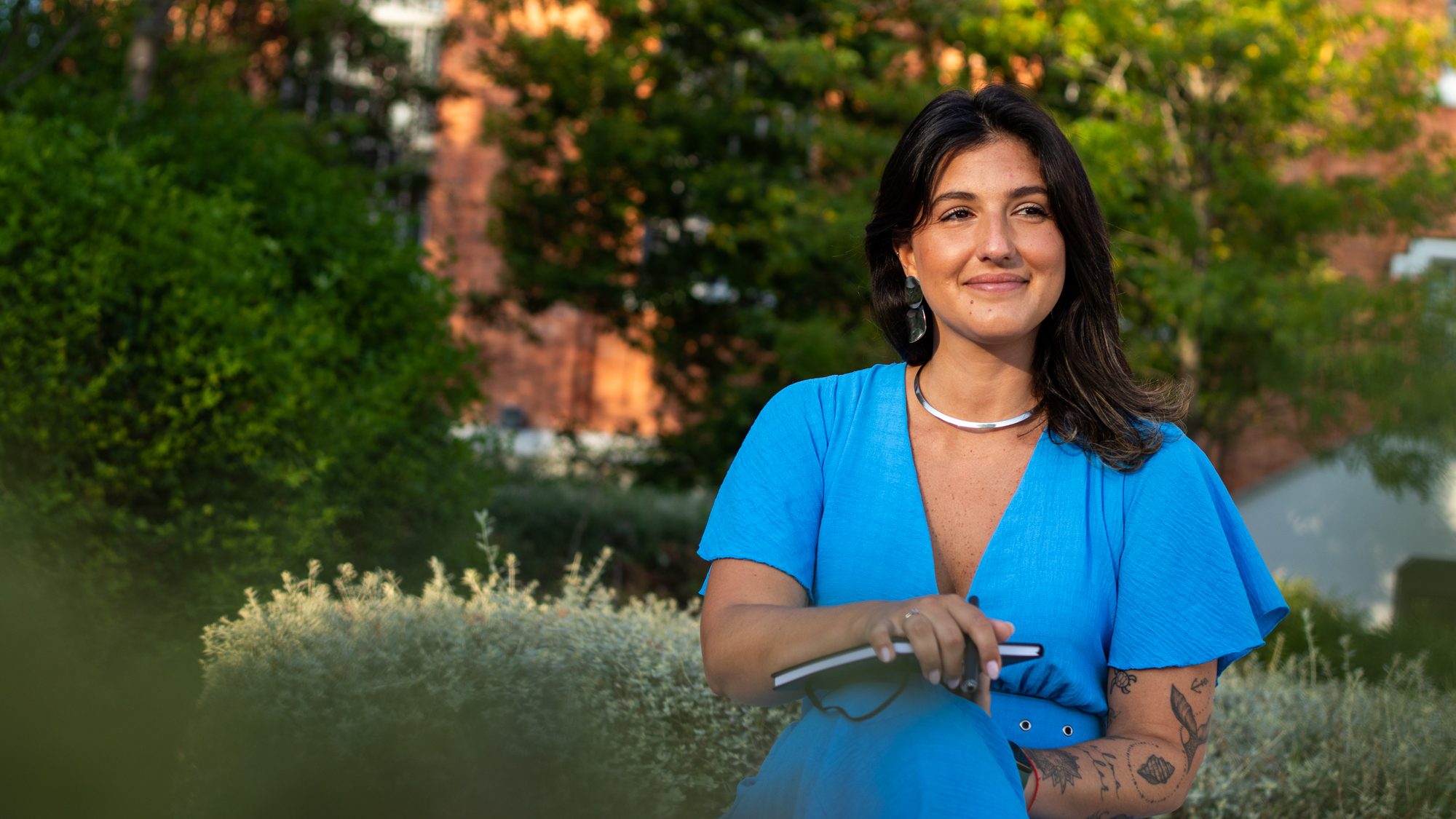 Carol Ferreira sentada num jardim ao fim da tarde, com um caderno na mão
